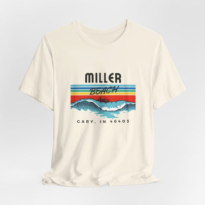 The Miller Beach 46403 Surf Style - Unisex Jersey Short Sleeve Tee by Printify features a retro surf-inspired design on a yellow background. The shirt displays "MILLER BEACH" above waves with a skyline illustration, while "Cary, IN 46403" is printed below the waves. The vibrant design also includes colorful stripes in shades of blue, red, and orange.