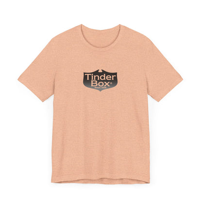 A light blue Printify "The Tinder Box 1980s" unisex jersey short sleeve tee featuring the "Tinder Box" logo in the center. The logo consists of a dark shield with the words "Tinder Box" in white text, with a small flame icon replacing the dot above the "i".