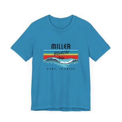 The Miller Beach 46403 Surf Style - Unisex Jersey Short Sleeve Tee by Printify features a retro surf-inspired design on a yellow background. The shirt displays "MILLER BEACH" above waves with a skyline illustration, while "Cary, IN 46403" is printed below the waves. The vibrant design also includes colorful stripes in shades of blue, red, and orange.