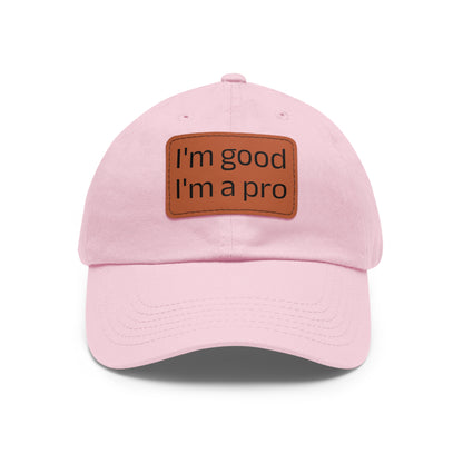 The Printify Dad Hat with Leather Patch (Rectangle) is a black, six-panel low-profile baseball cap made from bio-washed chino twill. This personalized Dad hat features a curved brim, visible stitching details, and a rectangular leather patch on the front that reads "I'm good I'm a pro" in grey text.