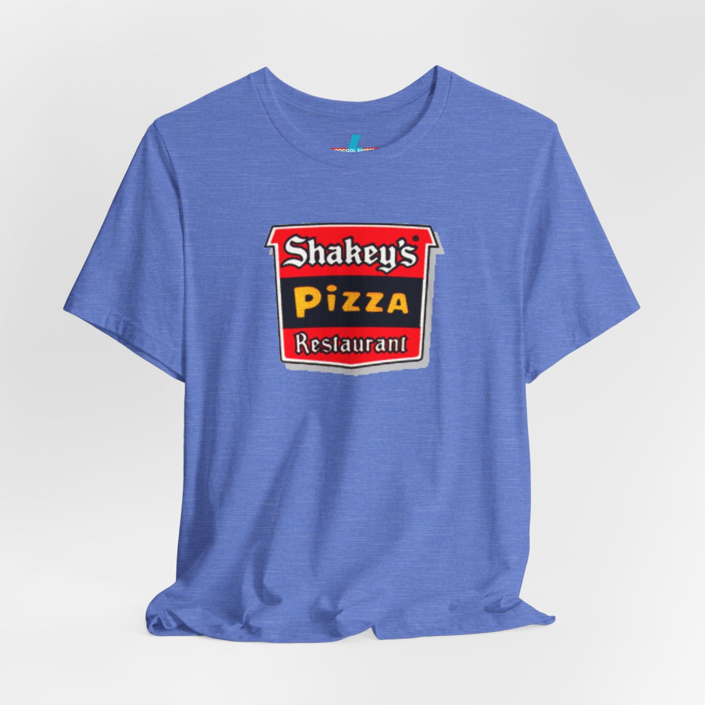 A black Shakey's Pizza - 1980s Retro Logo - Unisex T-Shirt by Printify hangs against a white background. The shirt features a colorful graphic with the text "Shakey's Pizza Restaurant" in white, yellow, and black lettering on a red background, resembling vintage pizza joints signage. This retro tee brings nostalgic vibes of classic pizzerias.