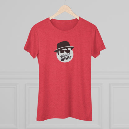 A cozy red t-shirt, the Miller Wiffel Ball - Blues Brothers - Women's Triblend Tee by Printify, features a graphic of a masked face wearing a fedora hat and sunglasses, along with the text "Miller Wiffle." The t-shirt is displayed on a wooden floor, paired with a denim jacket, white sneakers, and a potted green plant to create a vintage look.