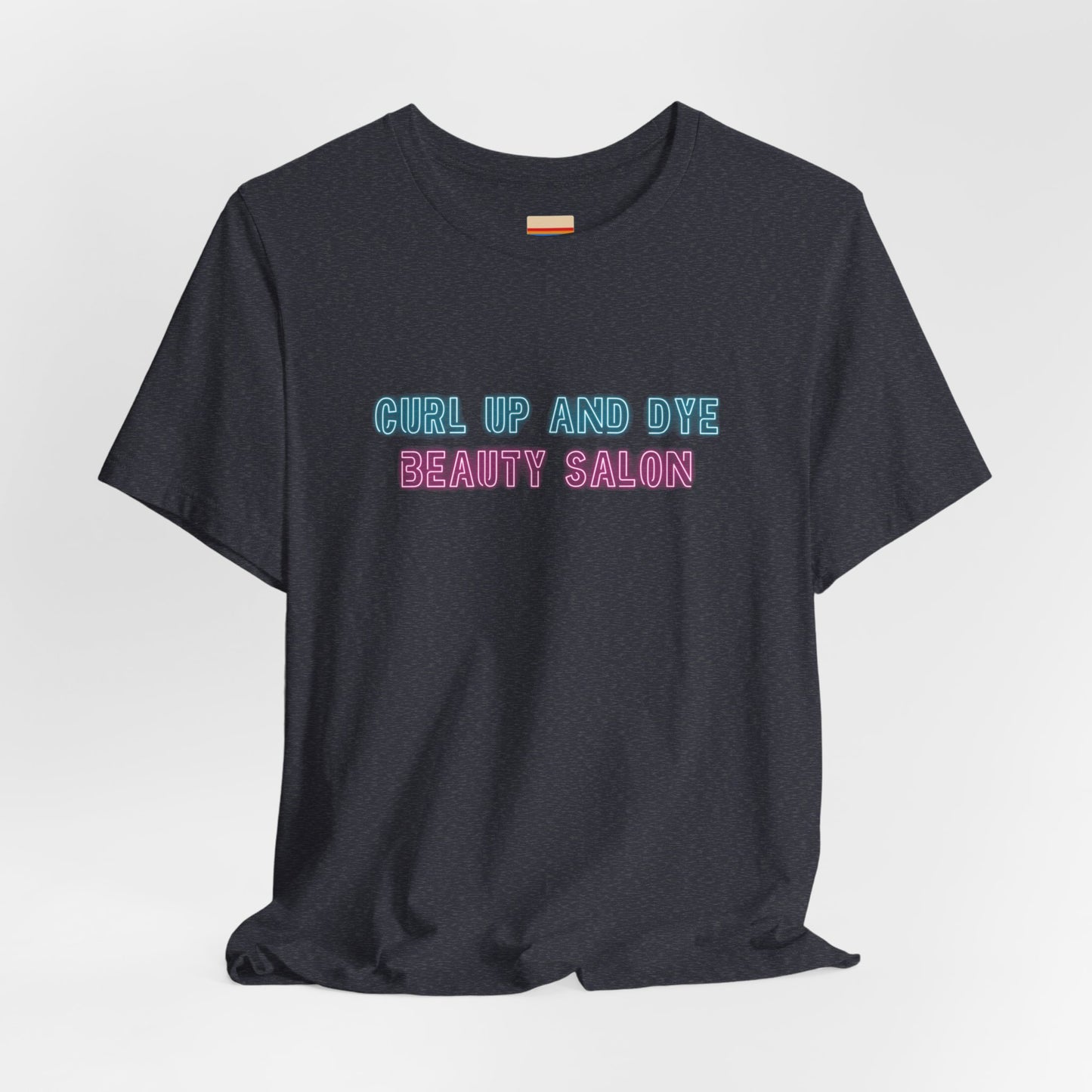 Introducing the Blues Brothers Curl Up and Dye Beauty Salon Unisex Jersey Short Sleeve Tee by Printify. This dark T-shirt features a nostalgic design with light blue and pink text that reads "CURL UP AND DYE BEAUTY SALON," reminiscent of a classic Blues Brothers tee. Crafted from 100% Airlume cotton, it is displayed against a plain light background.