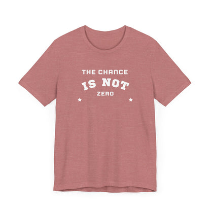 Folded light red Unisex Jersey Short Sleeve Tee from Printify, featuring bold white text that reads "THE CHANCE IS NOT ZERO" along with two star illustrations. This motivational T-shirt, made from breathable fabric, is neatly stacked with another identical shirt underneath.