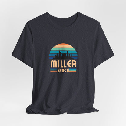 The Printify Miller Beach Chicago Skyline - Unisex Jersey Short Sleeve Tee is a light blue T-shirt featuring a stylized graphic of the Chicago skyline against a setting sun with gradient shades of blue and orange. Below the graphic, "Miller Beach" is printed in bold, yellow letters.