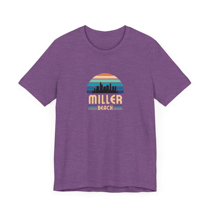 A brown unisex jersey short sleeve tee called "Miller Beach Chicago Skyline" from Printify features a vintage-style design with a sunset, the Chicago skyline, and "Miller Beach" in bold letters. The design incorporates shades of blue, orange, and yellow and is displayed against a plain white background.