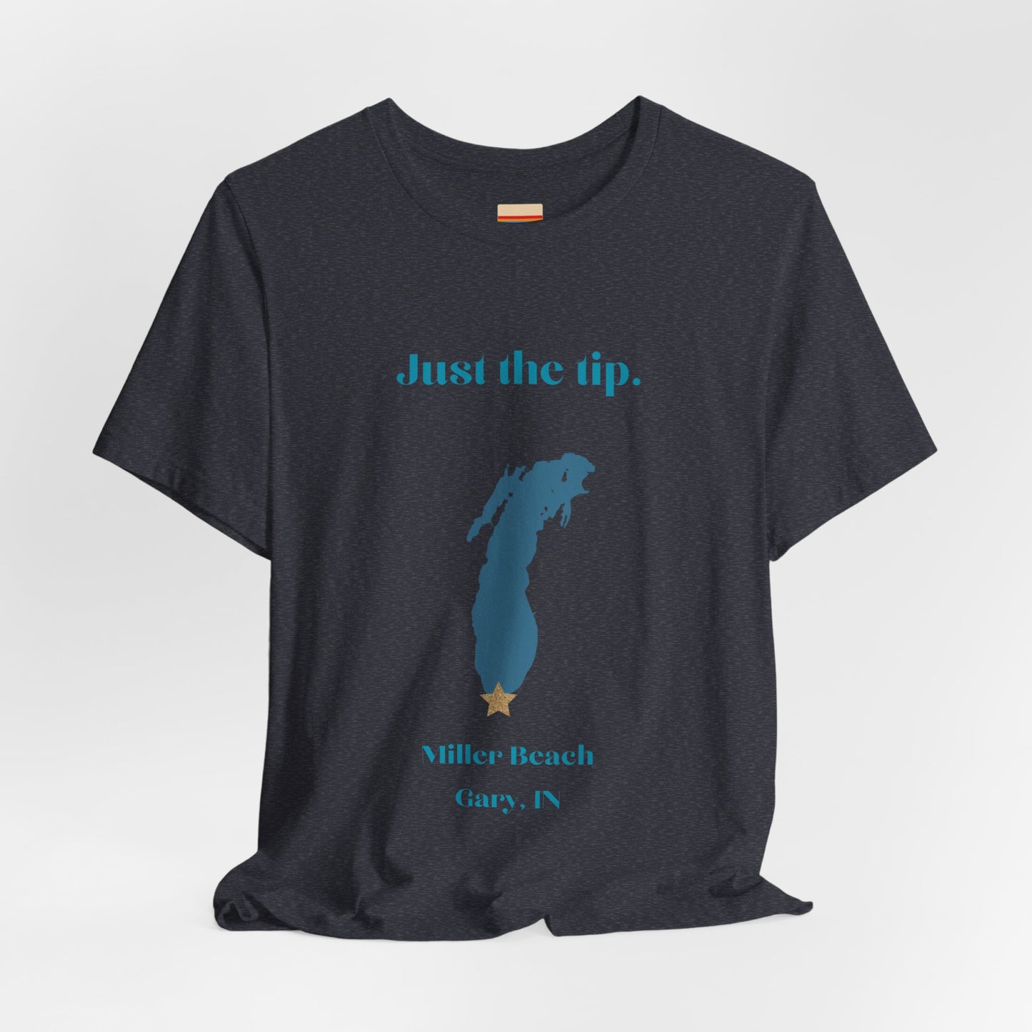 The Just the Tip - Miller Beach Unisex Jersey Short Sleeve Tee by Printify in yellow showcases text and a graphic design. The top displays "Just the tip" above a blue silhouette reminiscent of Indiana. At the bottom, it reads "Miller Beach" and "Gary, IN." Made from soft Airlume combed cotton, this tee offers both comfort and style.