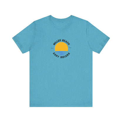 The Miller Beach Gary Indiana EST 1851 - Unisex Jersey Short Sleeve Tee by Printify is a classic blue unisex shirt featuring a vibrant graphic design of a yellow sun setting over blue waves. The text surrounding the artwork reads "Miller Beach" at the top and "Gary Indiana" at the bottom, making it an ideal tribute to this cherished location.