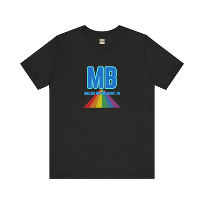 The Miller Beach Pride - Unisex Jersey Short Sleeve Tee by Printify is a white shirt made from 100% Airlume combed cotton. It showcases a design with large, bold blue letters "MB" at the top. Beneath it, the text "MILLER BEACH GARY, IN" is written in blue. A colorful, triangular rainbow graphic extends downward from the text, symbolizing Miller Beach pride.