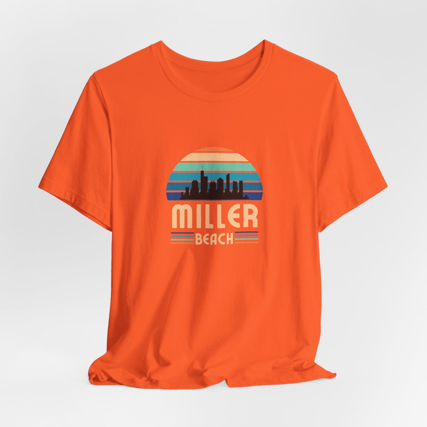 The Printify Miller Beach Chicago Skyline - Unisex Jersey Short Sleeve Tee is a light blue T-shirt featuring a stylized graphic of the Chicago skyline against a setting sun with gradient shades of blue and orange. Below the graphic, "Miller Beach" is printed in bold, yellow letters.