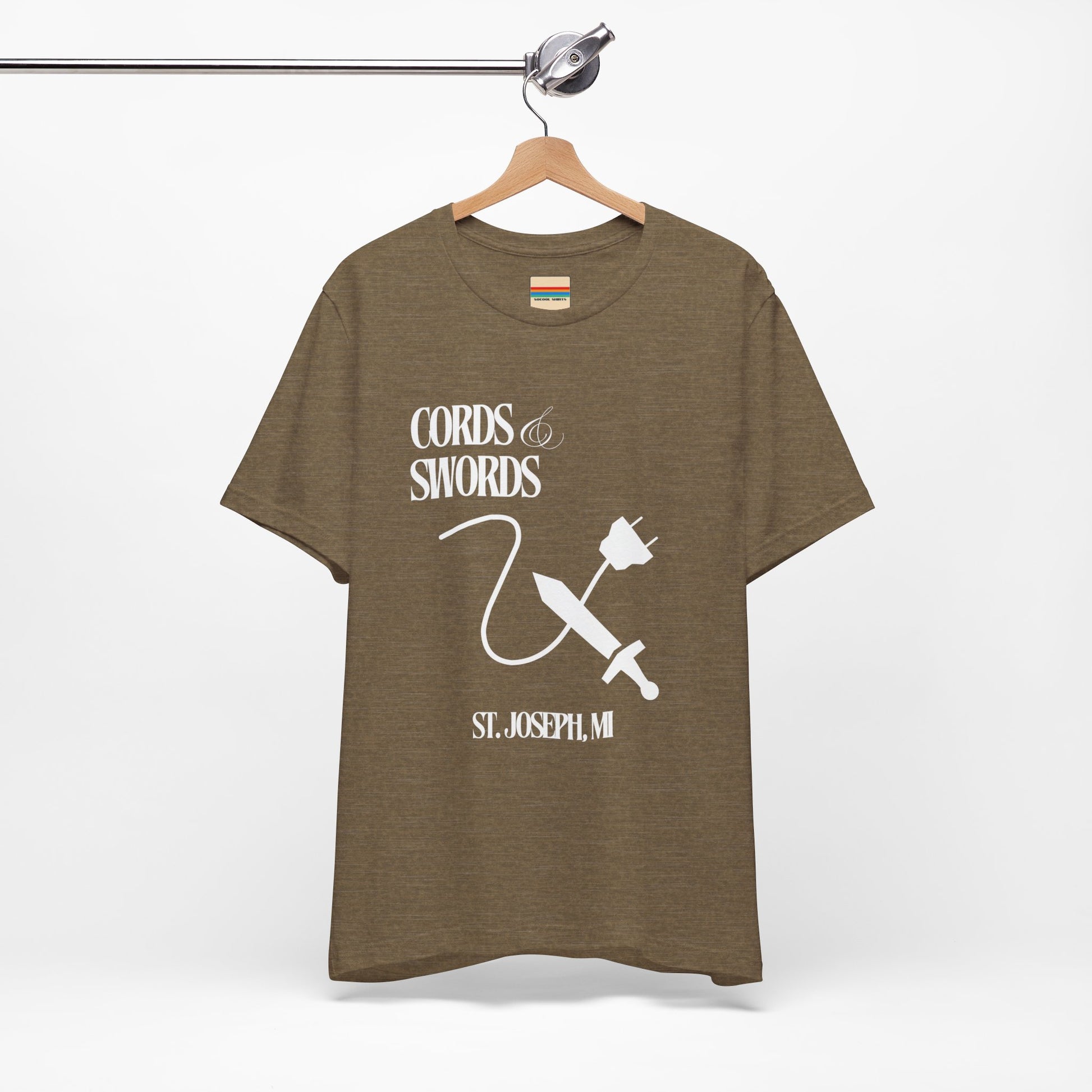 The SoCool Podcast - Cords & Swords Store T-Shirt by Printify is a vintage-inspired blue shirt that showcases a white graphic with the text "Cords & Swords" above illustrations of a crossed power cord and sword, along with "St. Joseph, MI" beneath. Ideal for tech enthusiasts, this design is centered on the front against a plain white background.