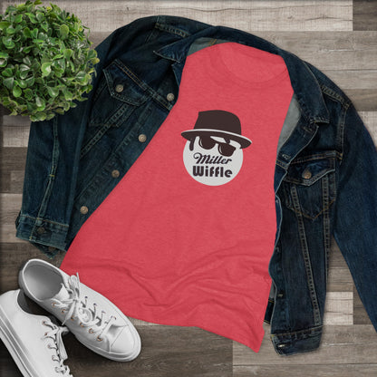 A cozy red t-shirt, the Miller Wiffel Ball - Blues Brothers - Women's Triblend Tee by Printify, features a graphic of a masked face wearing a fedora hat and sunglasses, along with the text "Miller Wiffle." The t-shirt is displayed on a wooden floor, paired with a denim jacket, white sneakers, and a potted green plant to create a vintage look.