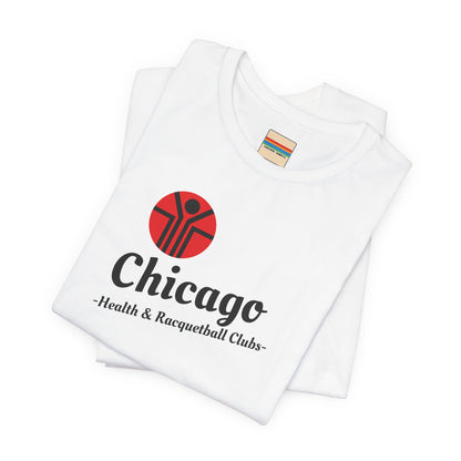 Two gray T-shirts are neatly folded on top of each other, with the top shirt showcasing the text "Chicago Health & Racquetball Clubs" in black below a red logo featuring a person with raised arms inside a circular design. This retro-inspired tee, named "Chicago Health Clubs 1980s Retro - Unisex Jersey Short Sleeve Tee" by Printify, is perfect for any fan of Chicago Health Clubs.