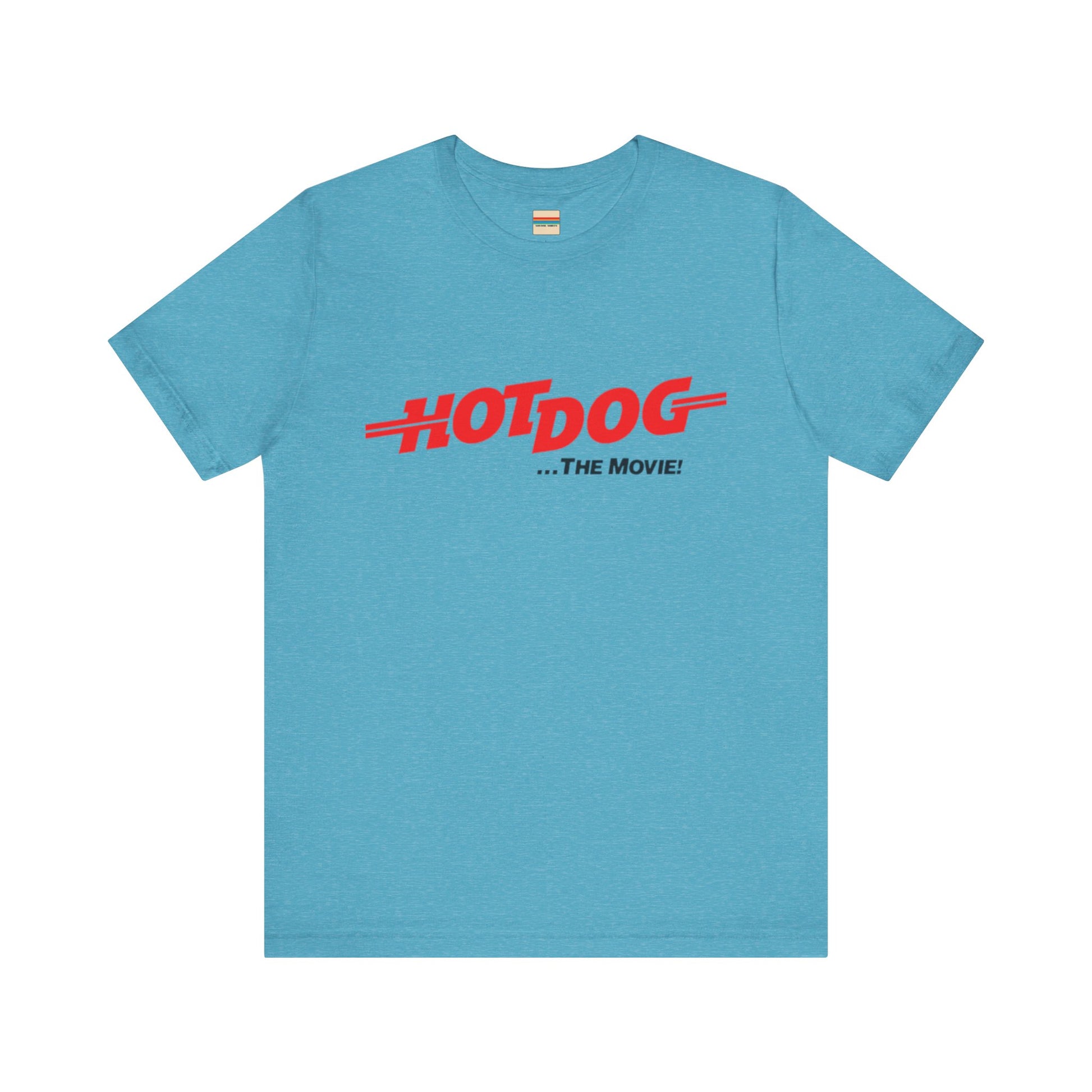 A smiling man and woman interact while wearing matching yellow "Hot Dog The Movie 1984 - Unisex Jersey Short Sleeve Tee" by Printify, featuring bold red "HOT DOG THE MOVIE" text. Their vibrant tees perfectly complement their blue jeans, with the man casually having his hands in his pockets and the woman resting one hand on his shoulder.