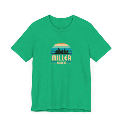 A brown unisex jersey short sleeve tee called "Miller Beach Chicago Skyline" from Printify features a vintage-style design with a sunset, the Chicago skyline, and "Miller Beach" in bold letters. The design incorporates shades of blue, orange, and yellow and is displayed against a plain white background.