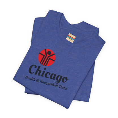 Two gray T-shirts are neatly folded on top of each other, with the top shirt showcasing the text "Chicago Health & Racquetball Clubs" in black below a red logo featuring a person with raised arms inside a circular design. This retro-inspired tee, named "Chicago Health Clubs 1980s Retro - Unisex Jersey Short Sleeve Tee" by Printify, is perfect for any fan of Chicago Health Clubs.