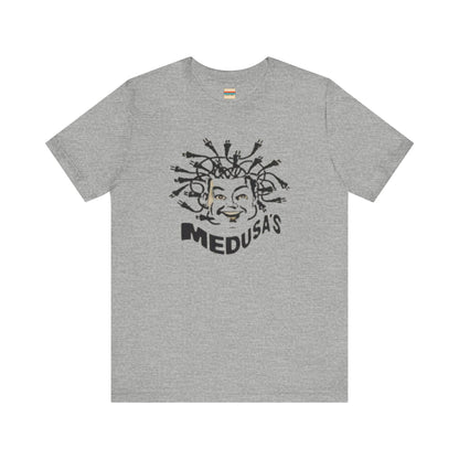 A cream-colored unisex jersey short sleeve tee from Printify, titled "Medusa's 1980s Dance Club Chicago," features a black and white illustration of a cartoonish Medusa head. The soft cotton design showcases numerous snakes as hair with a smiling face. Below, the word "MEDUSA'S" is printed in bold, playful font.