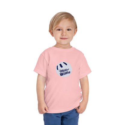 A young child with light hair stands against a plain white background, smiling while wearing a vibrant yellow Printify short sleeve tee named "Miller Wiffel Ball OG Logo - Toddler Short Sleeve Tee." The shirt features the "Miller Wiffle" text and a wiffle ball graphic on the front. The child is also dressed in blue pants.