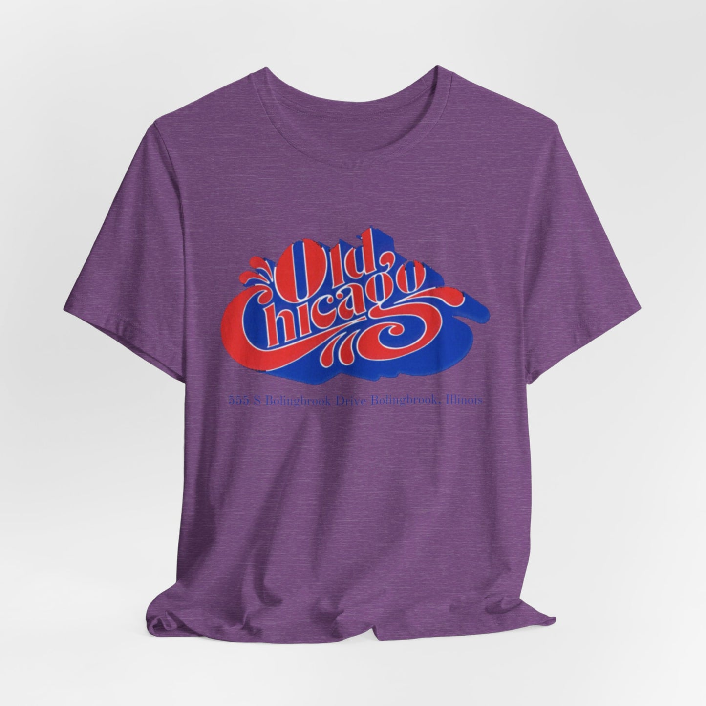 The "Old Chicago Mall Bolingbrook 1980s Retro - Unisex Jersey Short Sleeve Tee" from Printify is a gray T-shirt showcasing a vintage design with the text "Old Chicago" in blue and red. Beneath the main text, the address "355 S. Bolingbrook Drive, Bolingbrook, Illinois" appears in smaller font, evoking 80s nostalgia of the Old Chicago Mall. The shirt is displayed against a white background.