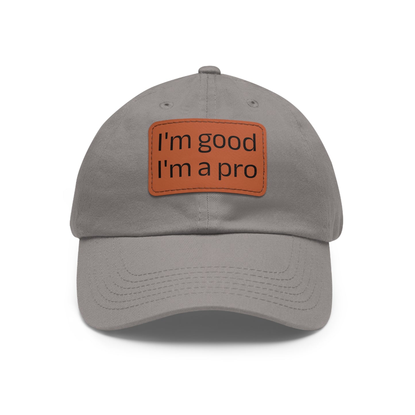 The Printify Dad Hat with Leather Patch (Rectangle) is a black, six-panel low-profile baseball cap made from bio-washed chino twill. This personalized Dad hat features a curved brim, visible stitching details, and a rectangular leather patch on the front that reads "I'm good I'm a pro" in grey text.