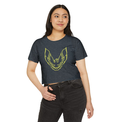 The Pontic Trans Am - Women's Festival Crop Top by Printify is a green heathered crop top featuring a large, stylized yellow eagle graphic with wings spread wide on the front, reminiscent of the Pontiac Phoenix Trans Am logo. With a simple crew neck and short sleeves, this top is ideal for vintage enthusiasts.