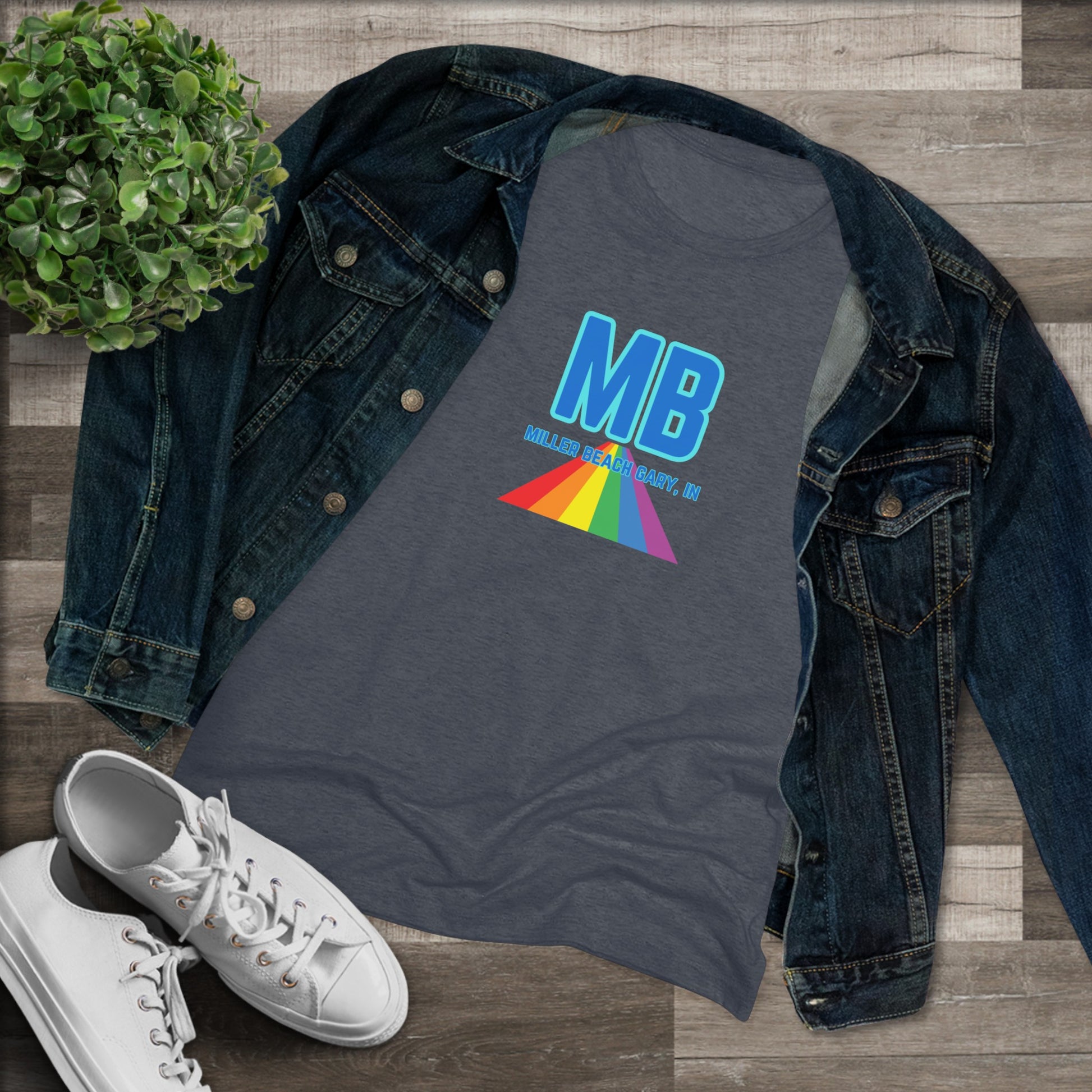 The Miller Beach Pride - Women's Triblend Tee by Printify is a dark gray, cozy t-shirt with a vintage look, featuring the text "MB" in large blue letters at the center. Below the letters, there is a rainbow-colored triangular design with "Millions & Binary, Inc." written in smaller text under the rainbow triangle.