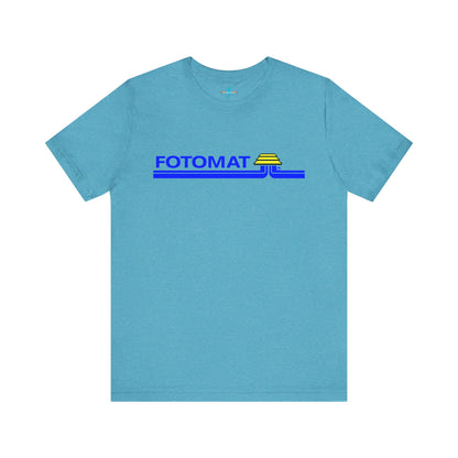 The Fotomat 1970s Retro T-Shirt by Printify is a dark gray short-sleeve shirt that features the word "FOTOMAT" in bold blue capital letters and a blue and yellow graphic design resembling layered lines and an upside-down triangle. This Tshirt captures the essence of 80s nostalgia with its centered, retro design.