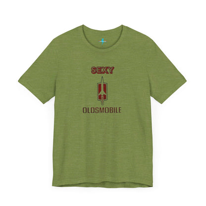 Introducing the Sexy Oldsmobile - Unisex Jersey Short Sleeve Tee by Printify, a light gray t-shirt featuring a striking graphic in the center. The design includes the word "SEXY" in bold red letters above a vertical Oldsmobile logo, underlined by the word "OLDSMOBILE" in red letters. This t-shirt is perfect for vintage car enthusiasts and comedy lovers alike, with its plain white background accentuating the bold design.