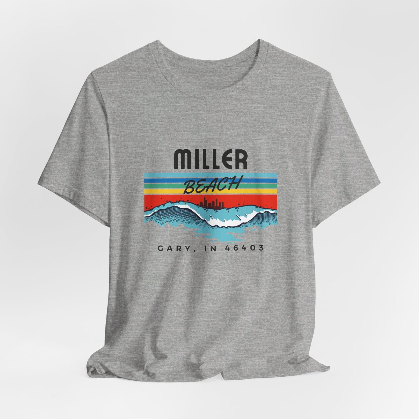 The Miller Beach 46403 Surf Style - Unisex Jersey Short Sleeve Tee by Printify features a retro surf-inspired design on a yellow background. The shirt displays "MILLER BEACH" above waves with a skyline illustration, while "Cary, IN 46403" is printed below the waves. The vibrant design also includes colorful stripes in shades of blue, red, and orange.