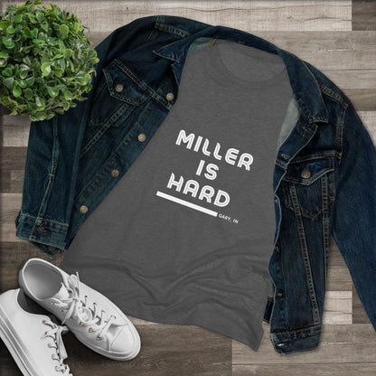 The Miller is Hard - Miller Beach Women's Triblend Tee by Printify features unique red coloring with white text that reads "MILLER IS HARD" and "GARY, IN" below, showcasing distinctive lettering spacing and alignment. Made from ultra-soft fabric, this shirt ensures a comfortable fit with a simple, casual design.