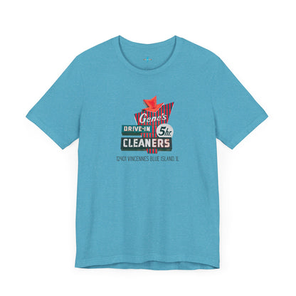 A unisex Jersey short sleeve tee from Printify featuring a light grey color with a retro-style graphic in the center. The design showcases text that reads "Gene's Drive In Cleaners, 5th," along with the address "12401 Vincennes Blue Island IL" in a blend of vintage fonts and colors, evoking the classic Chicago Fire-era vintage sign aesthetic.