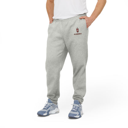 Gray Printify adidas fleece joggers with elastic waistband and cuffs, featuring the iconic Adidas logo on the upper left thigh and an "Oldsmobile - 1970s Logo" design on the right. Made with recycled polyester, they support the Better Cotton Initiative for a more sustainable future.