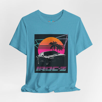 A Chevrolet Camaro iRoc Z Z28 T-Shirt 1980's by Printify, featuring a retro design with a black car, palm trees, and a sun setting in the background. The design includes geometric lines in neon colors and the text "IROC-Z" at the bottom, perfect for fans of the 1980s Chevy Camaro.