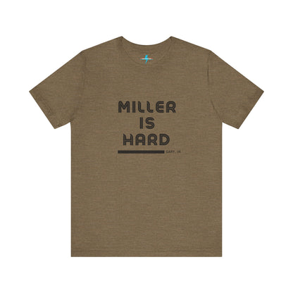 A unisex jersey short sleeve tee from Printify in burnt orange features the bold black text "MILLER IS HARD" on the chest, with "GARY, IN" written beneath in smaller black font. Perfect for showcasing Miller Beach's iconic spirit, this t-shirt is displayed against a plain white background.